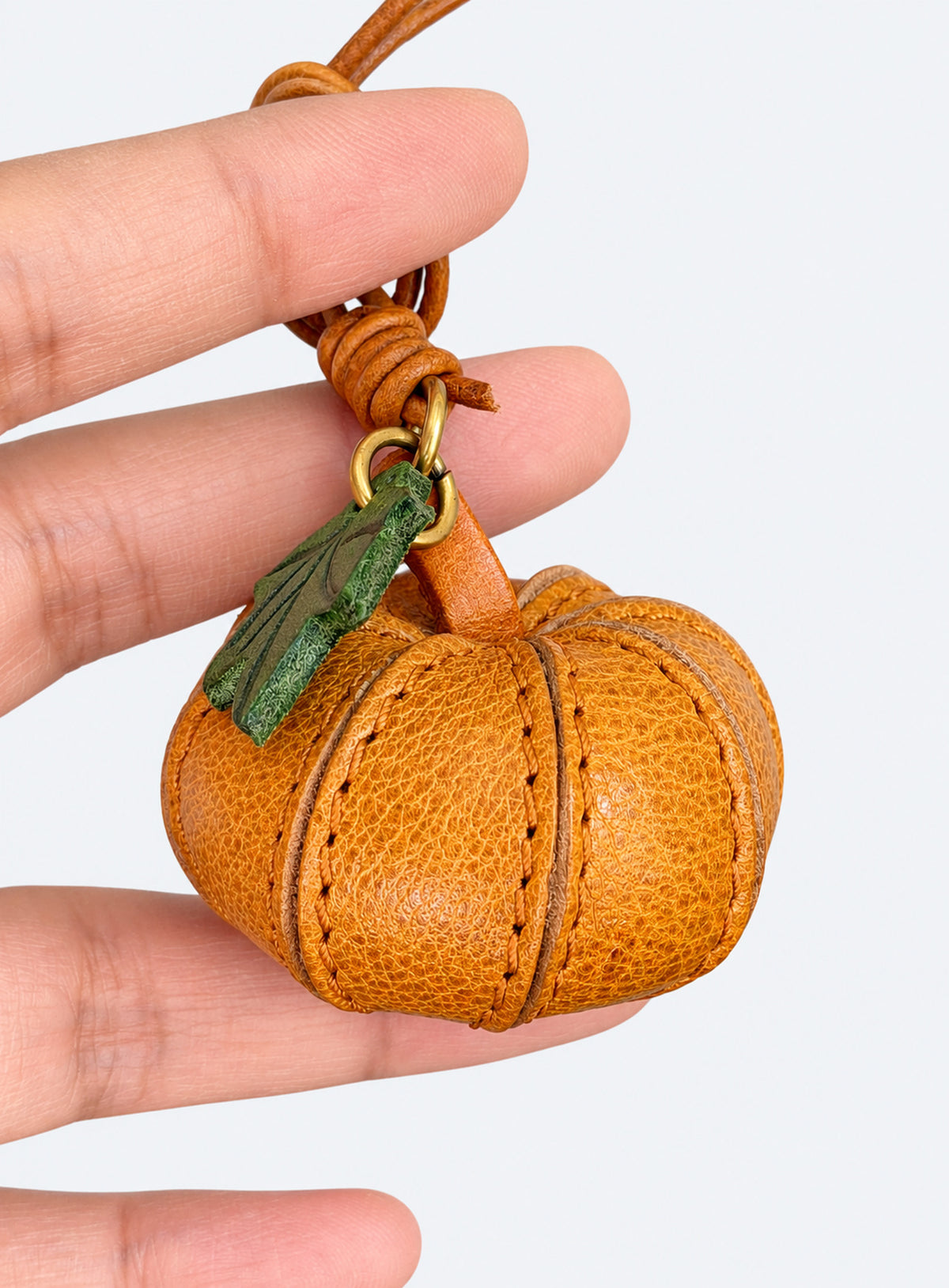 Pumpkin-shaped leather bag charm with stitched panels, a leaf accent, and a hanging loop (Cognac Brown)