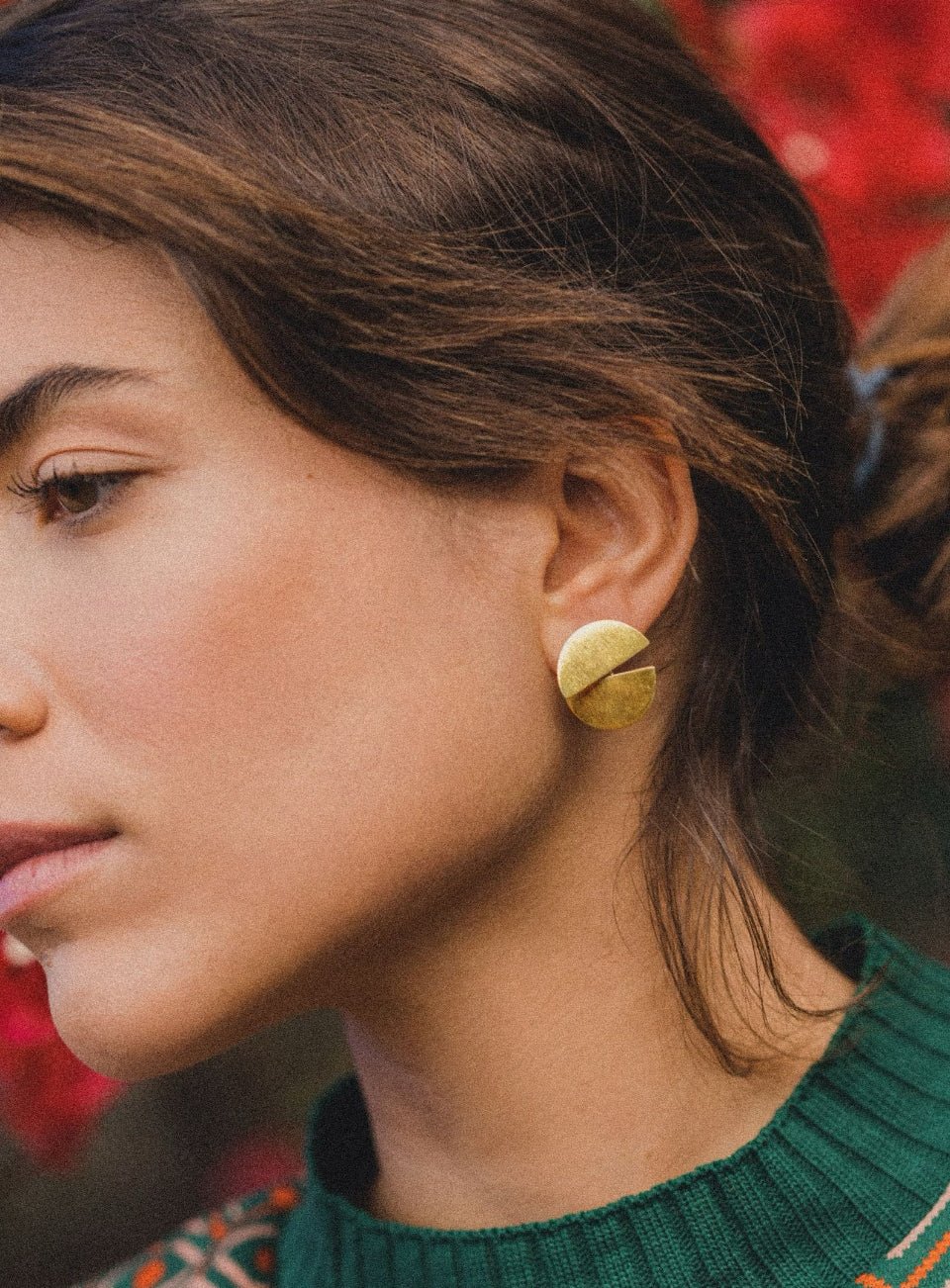 Close-up of a person wearing gold earrings with a blurred red background (Gold)