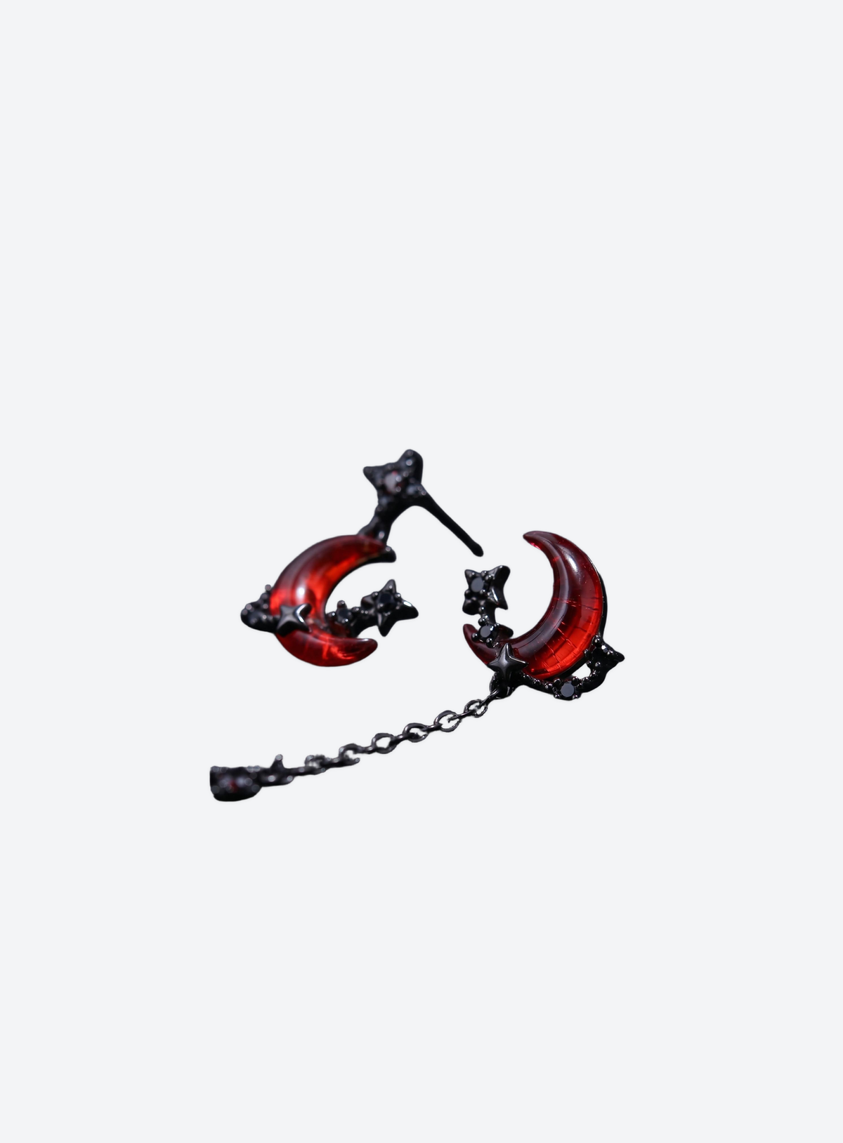 Asymmetrical red crescent moon and star dangle earrings on a light studio background