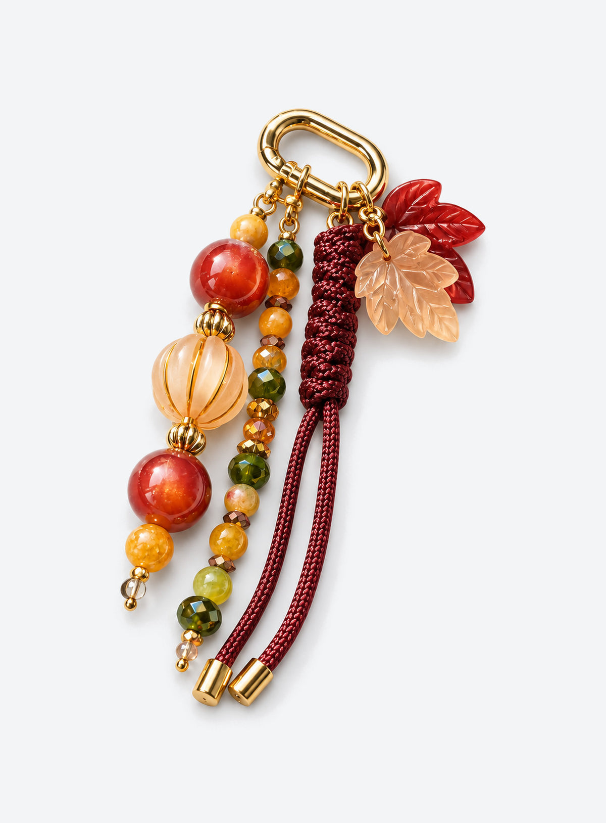 Bag charm with two leaf charms, red and amber-colored beads, burgundy woven cord and a gold-tone clasp