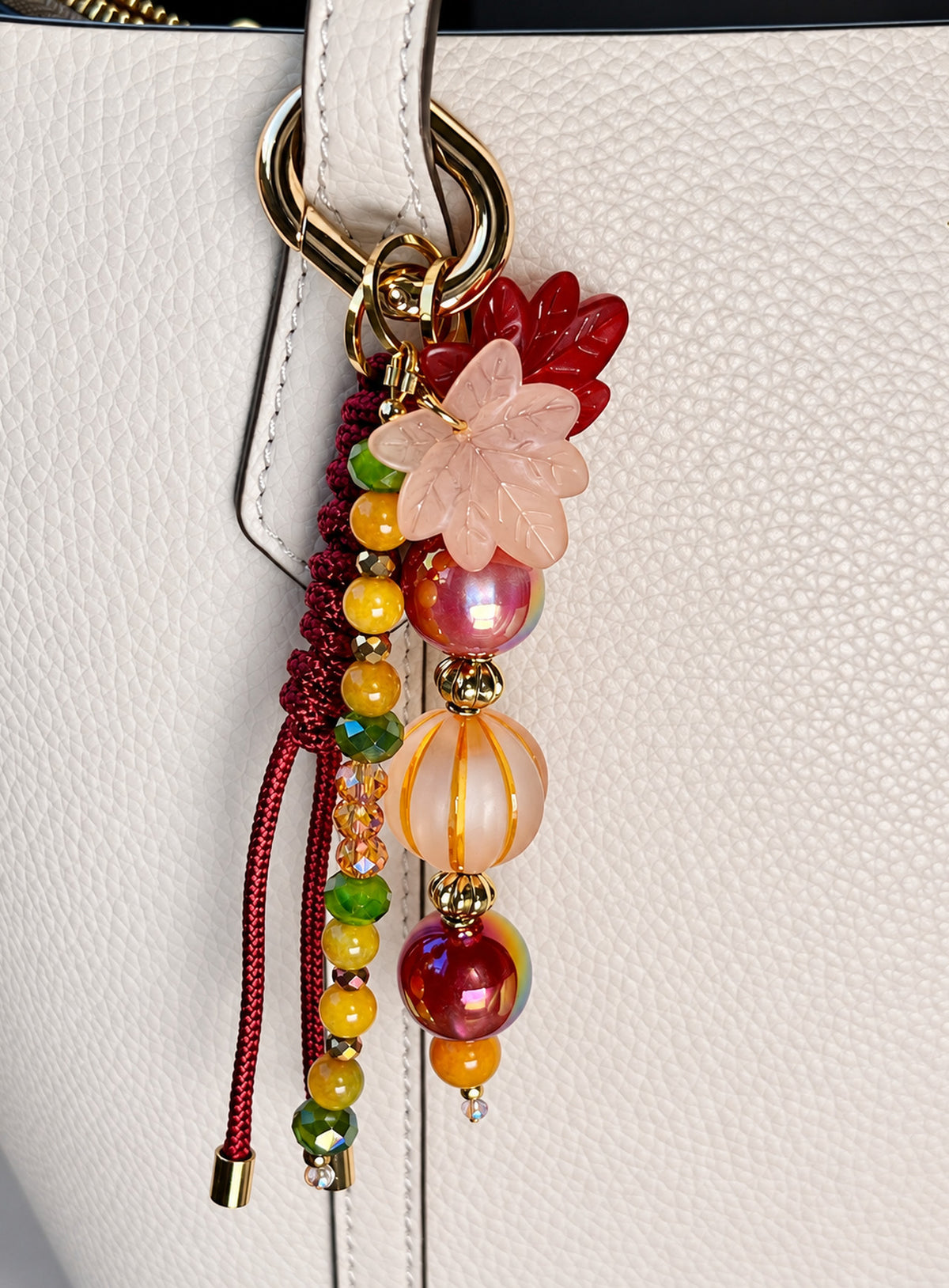 Bag charm with two leaf charms, red and amber-colored beads, burgundy woven cord and a gold-tone clasp