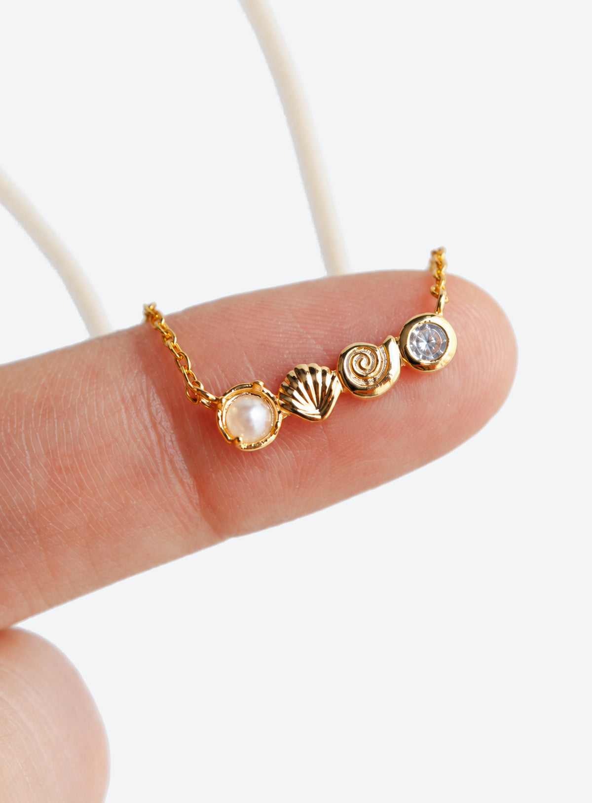 Delicate necklace with conch and scallop shell charms, a faux pearl and clear accents (Gold)