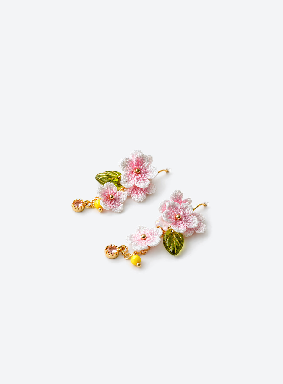 Pair of pink and white crochet cherry blossom earrings with green leaves and dangling bead accents