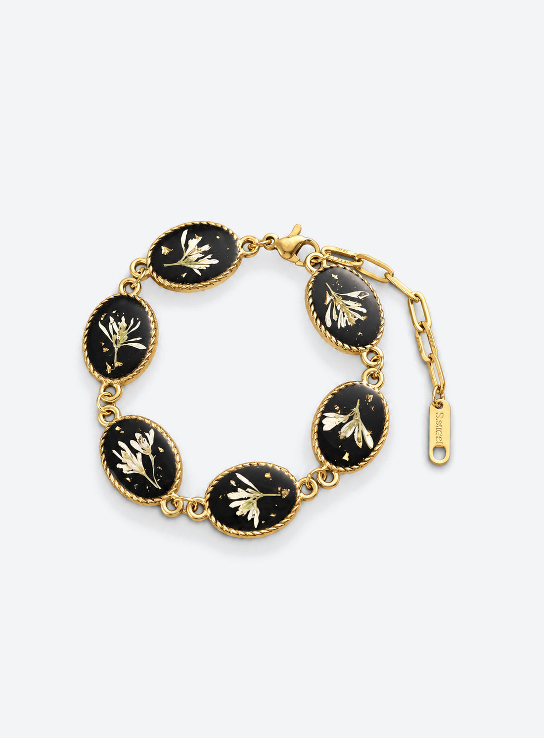 Linked oval bracelet charms with white dried flowers on black backgrounds and decorative vintage-inspired frames