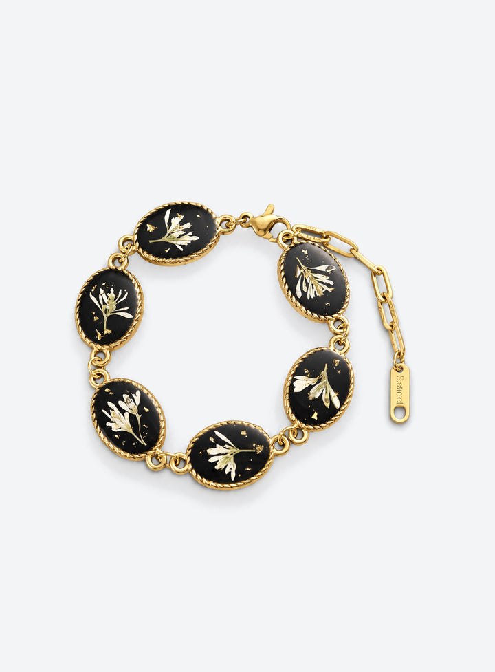 Linked oval bracelet charms with white dried flowers on black backgrounds and decorative vintage-inspired frames