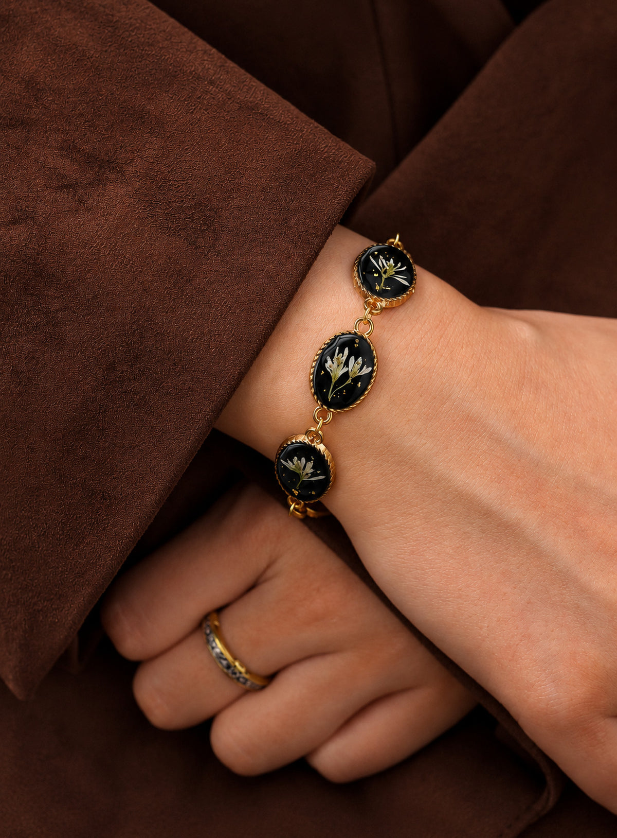 Linked oval bracelet charms with white dried flowers on black backgrounds and decorative vintage-inspired frames