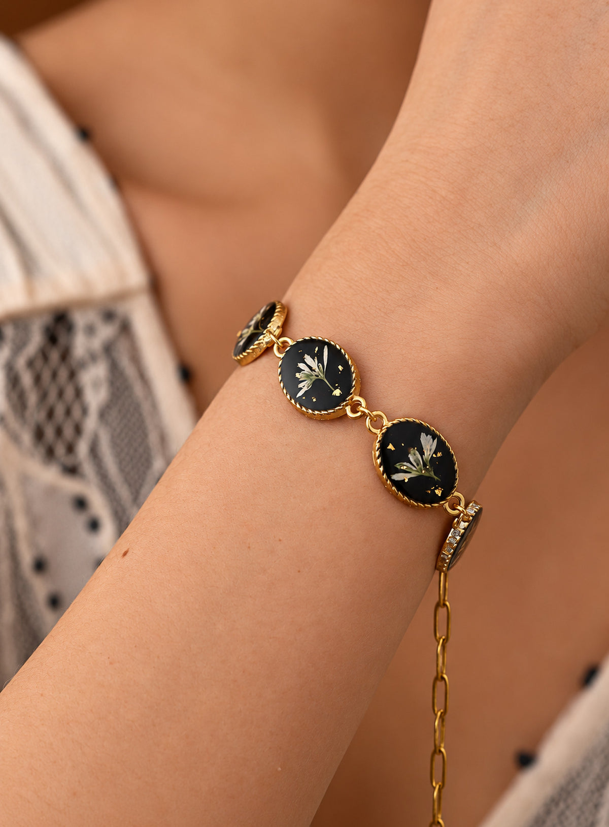 Linked oval bracelet charms with white dried flowers on black backgrounds and decorative vintage-inspired frames
