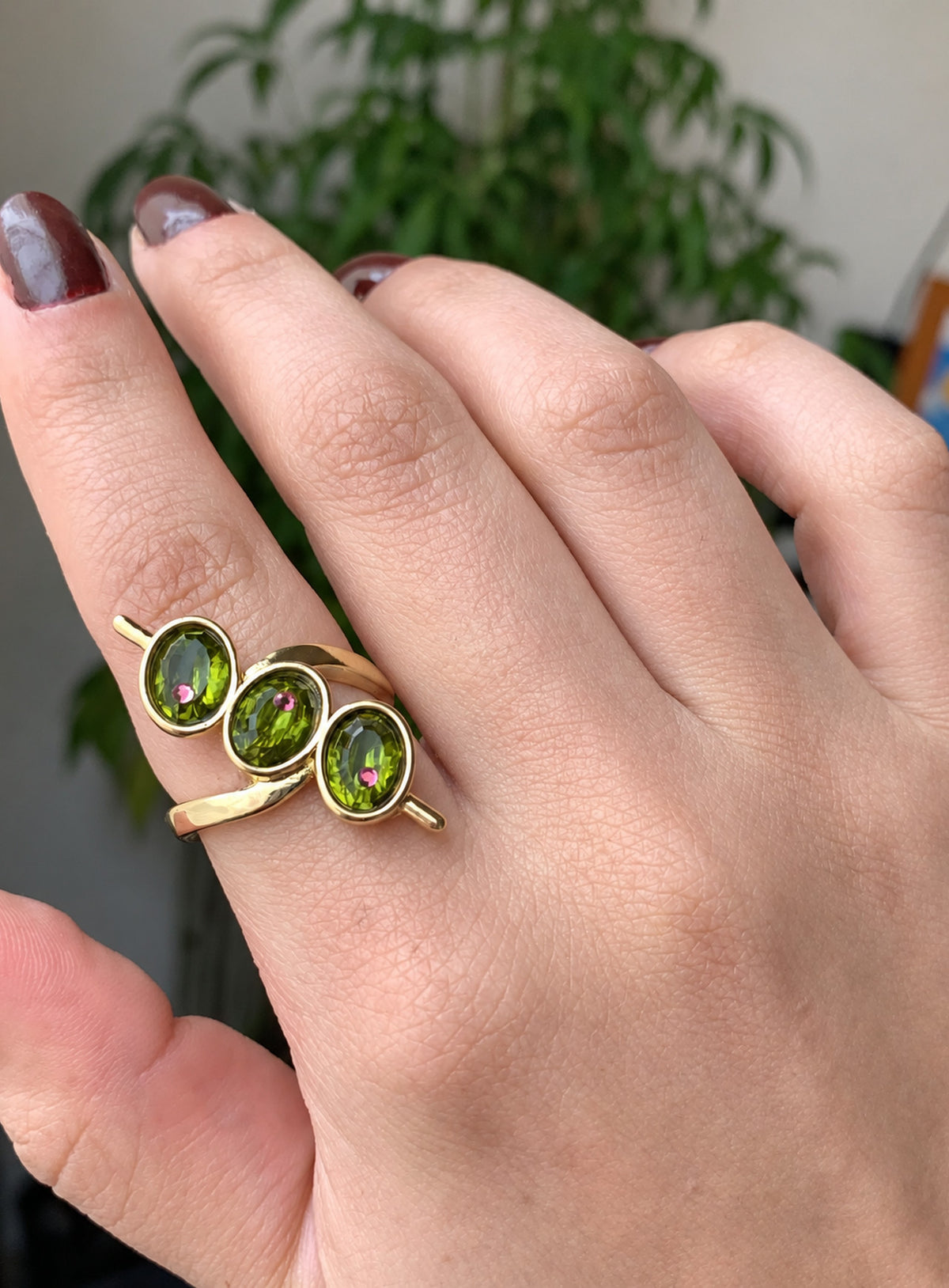 Gold-tone ring with three green oval faceted details, tiny red points and skewer-like side accents