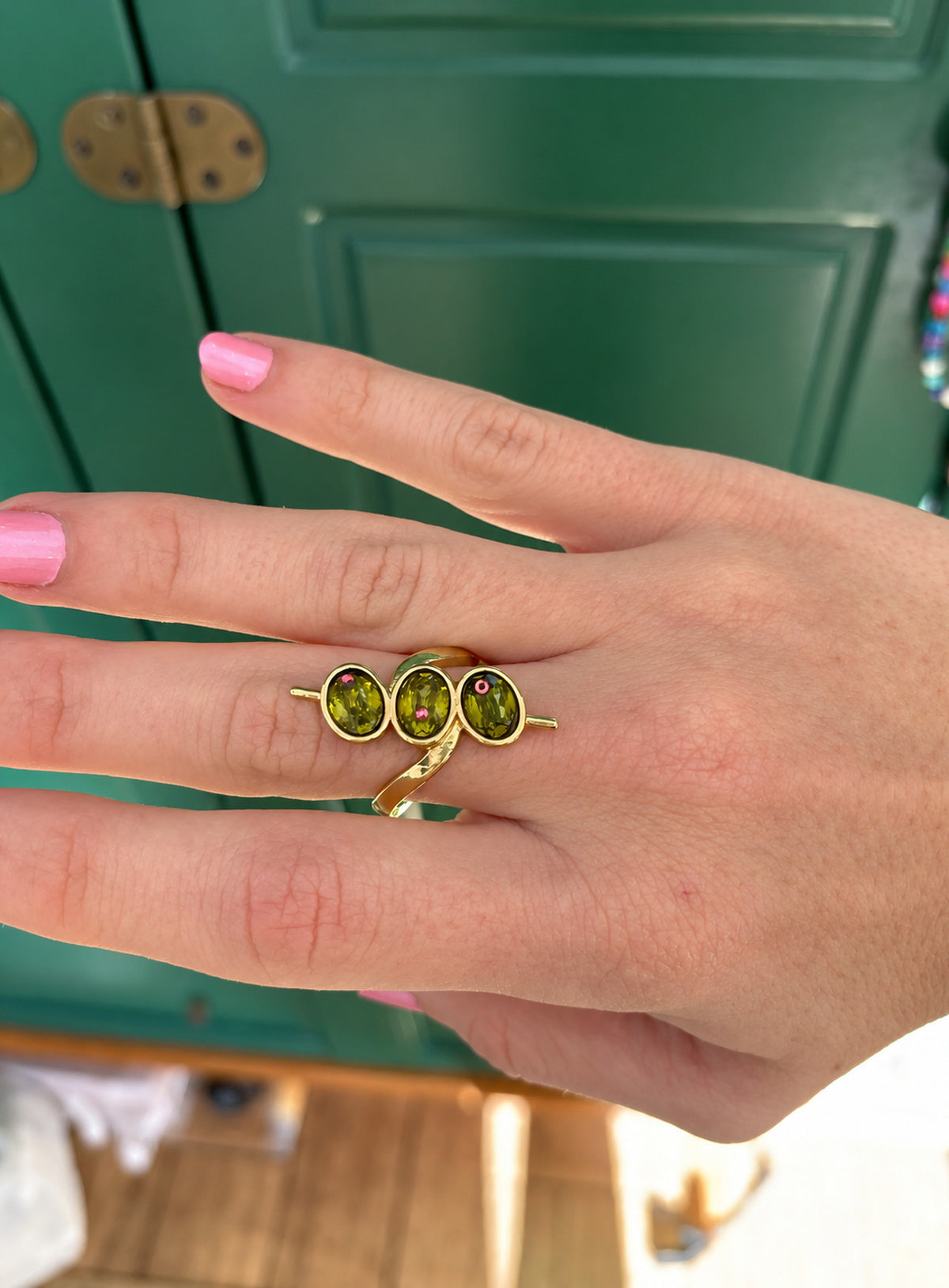 Gold-tone ring with three green oval faceted details, tiny red points and skewer-like side accents