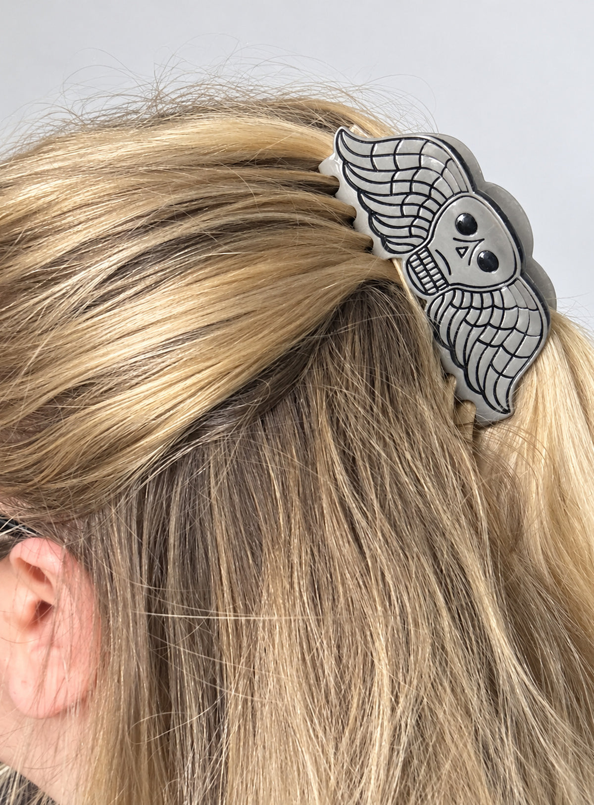 Small grey acetate hair claw with a winged skull design and dark outlines