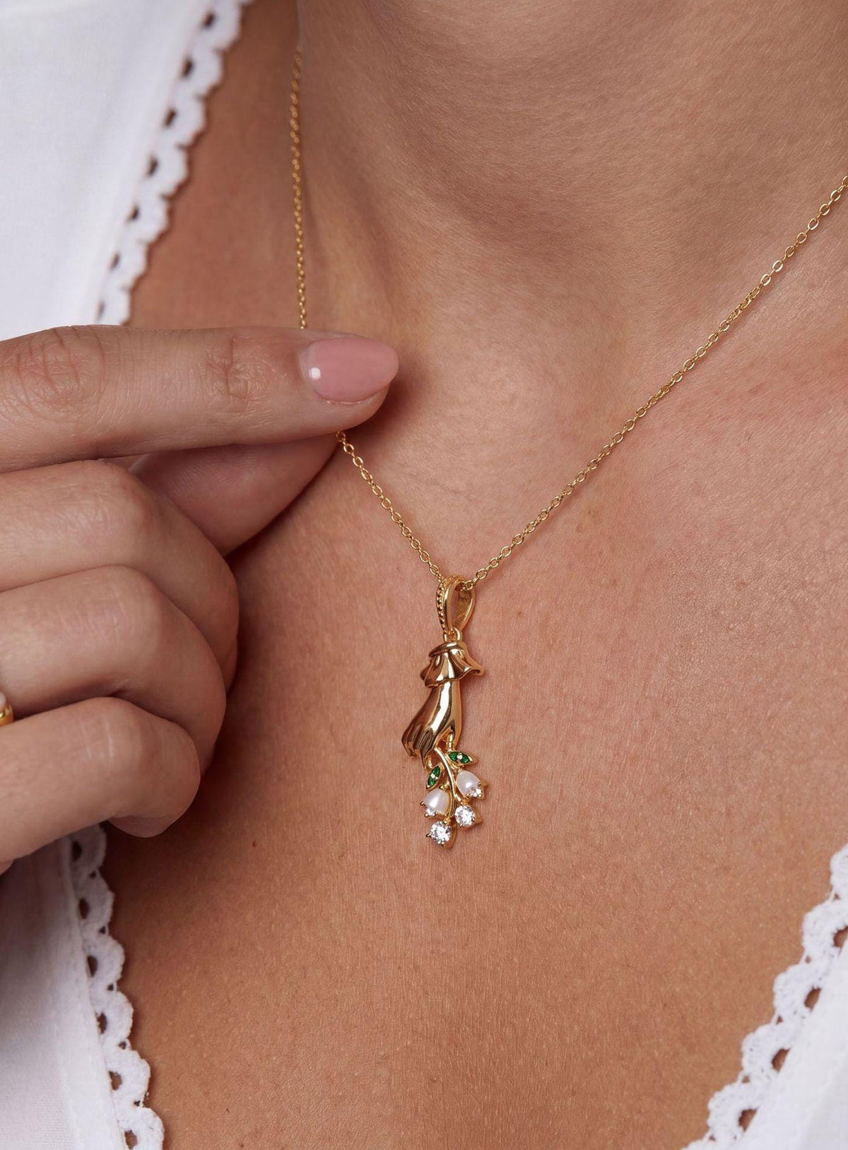 Necklace with a sculpted hand pendant holding a floral bouquet with crystal accents (May)