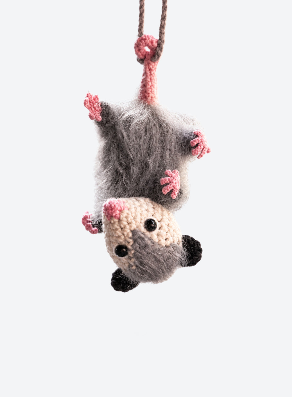 Grey opossum car charm hanging upside down by its tail with pink nose and paws