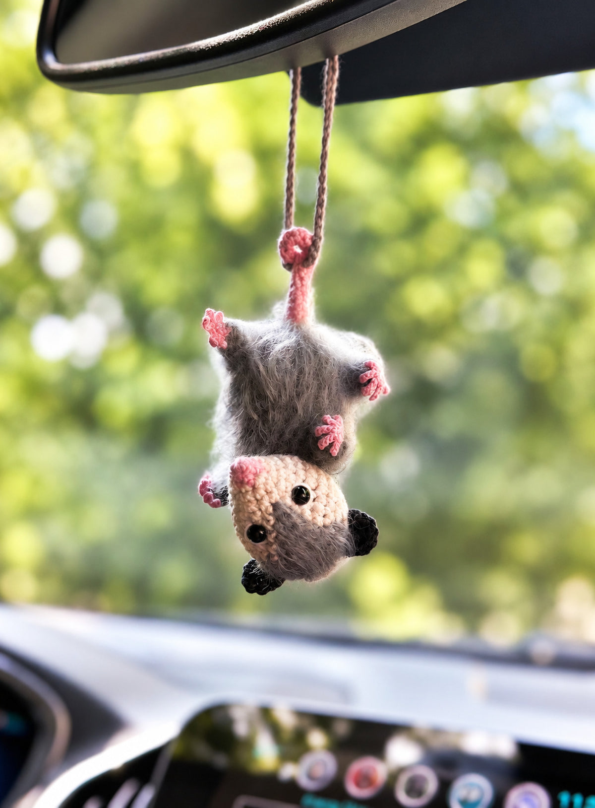 Grey opossum car charm hanging upside down by its tail with pink nose and paws