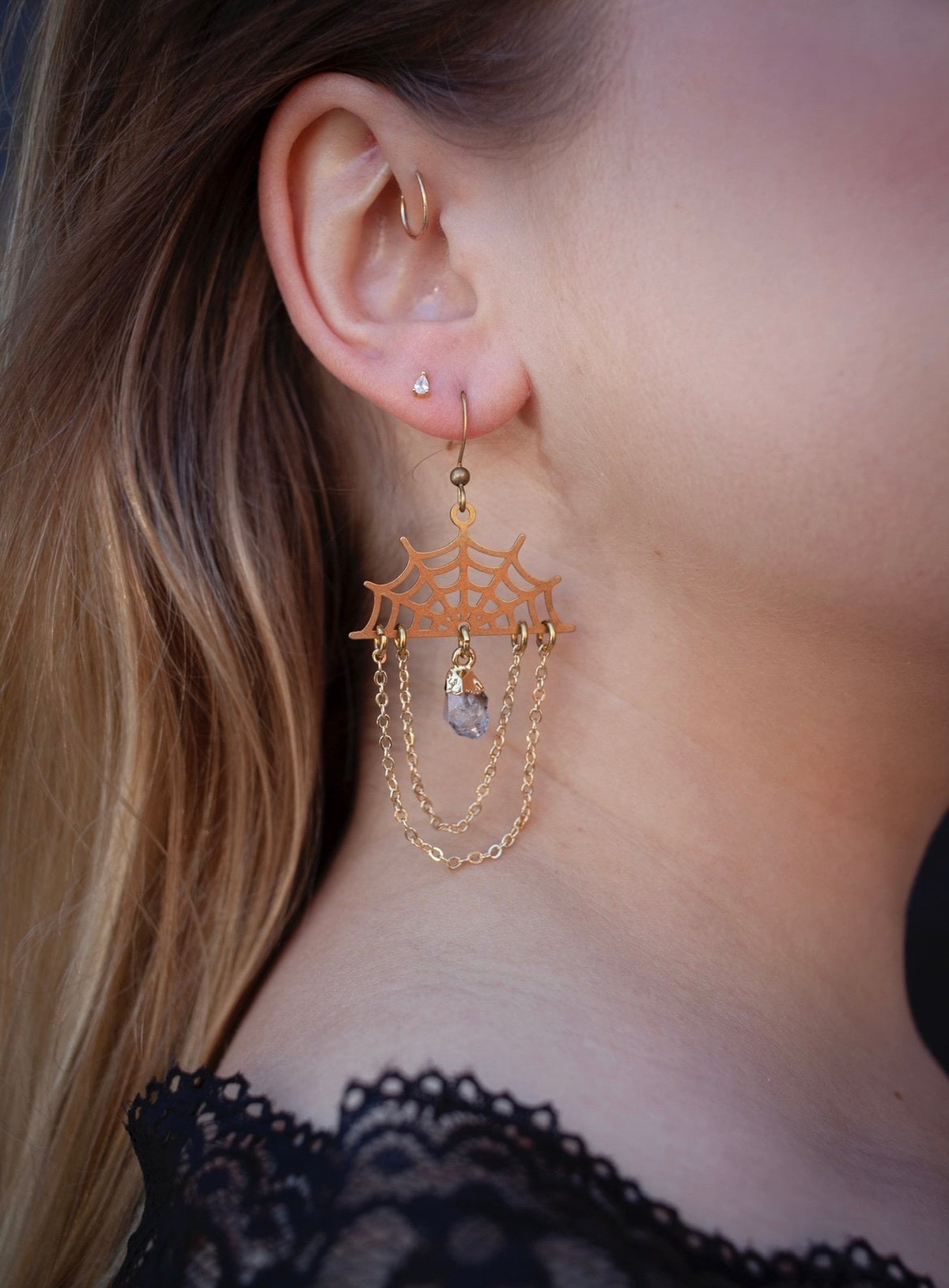 Gold-plated brass spider web earrings with Herkimer diamond charms on a studio background