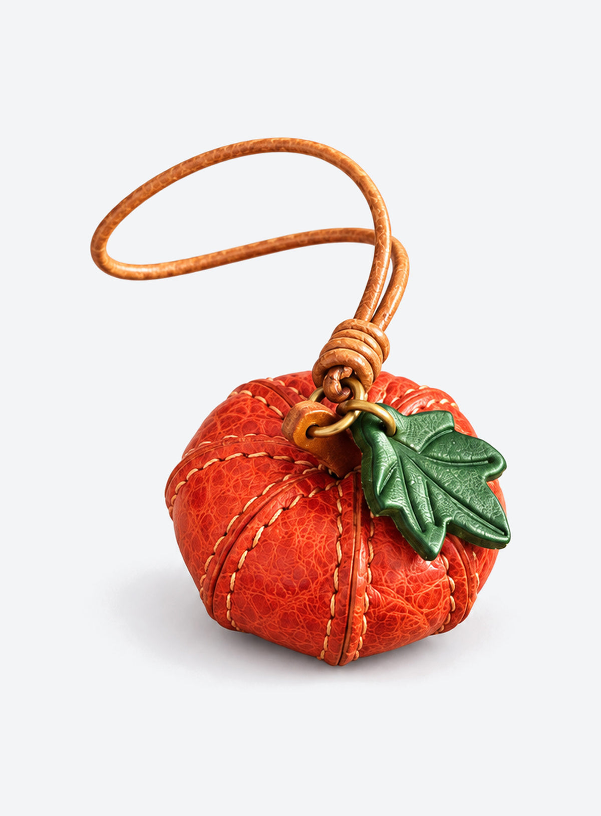 Pumpkin-shaped leather bag charm with stitched panels, a leaf accent, and a hanging loop