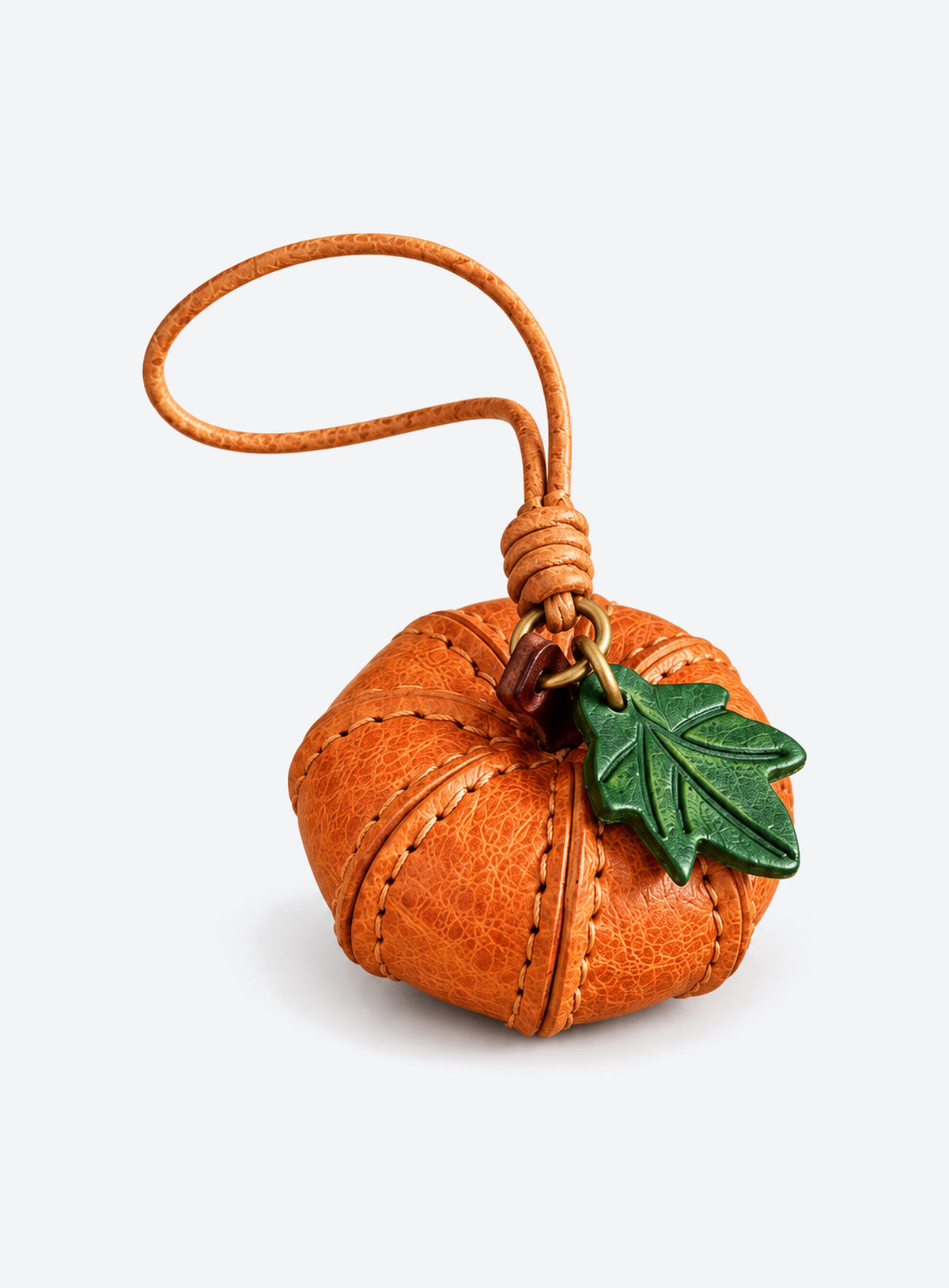 Pumpkin-shaped leather bag charm with stitched panels, a leaf accent, and a hanging loop