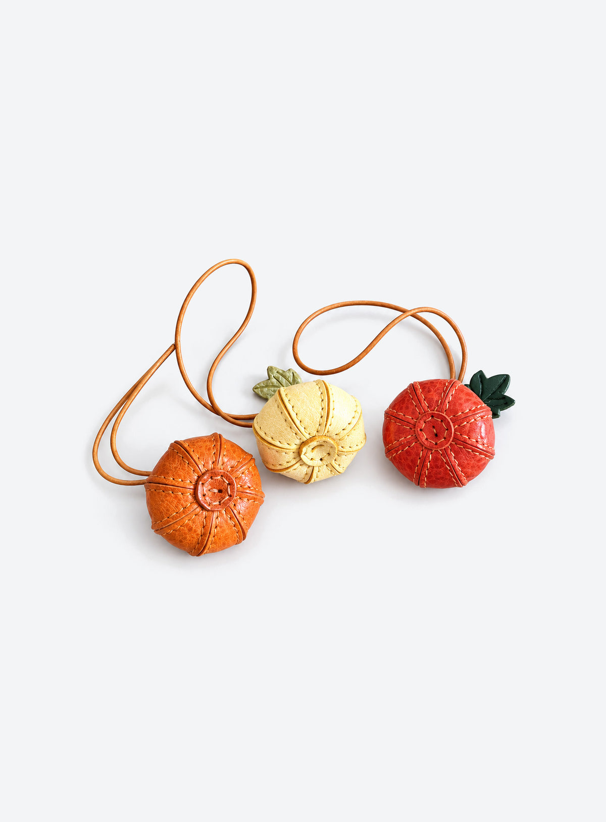 Pumpkin-shaped leather bag charm with stitched panels, a leaf accent, and a hanging loop