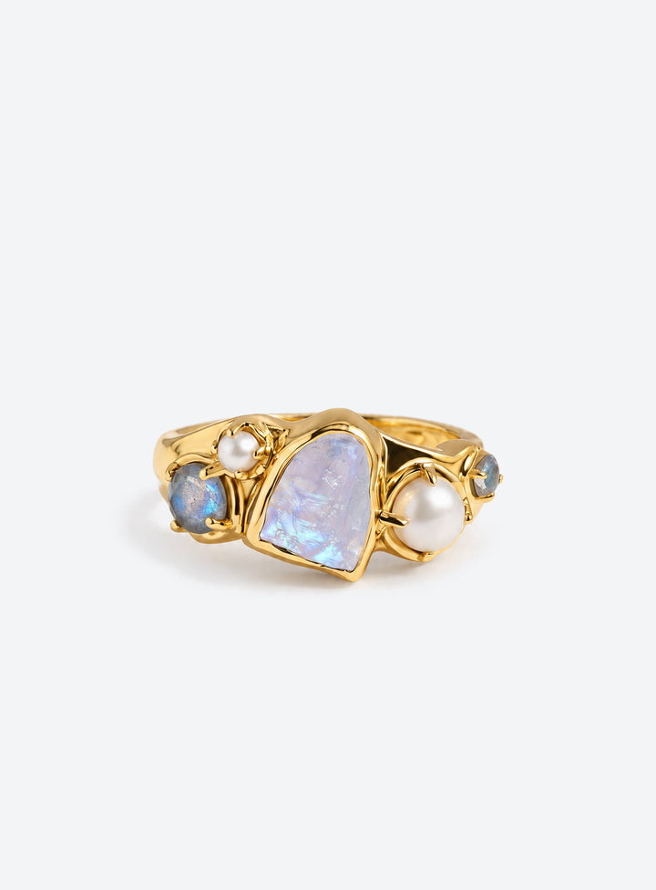 Gold-finish ring with a pale irregular moonstone, white pearls, and small blue-gray stones in an asymmetric cluster