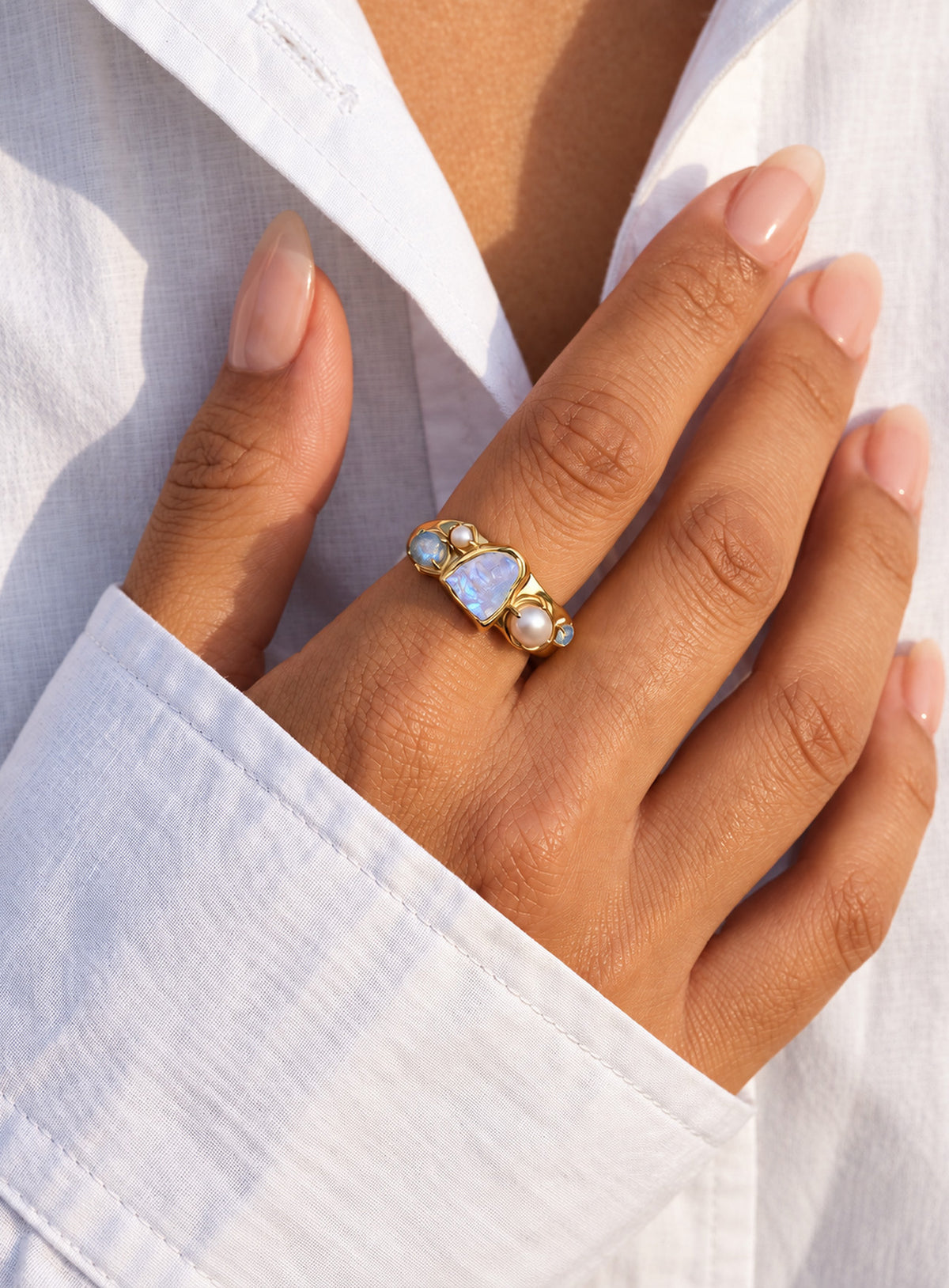 Gold-finish ring with a pale irregular moonstone, white pearls, and small blue-gray stones in an asymmetric cluster