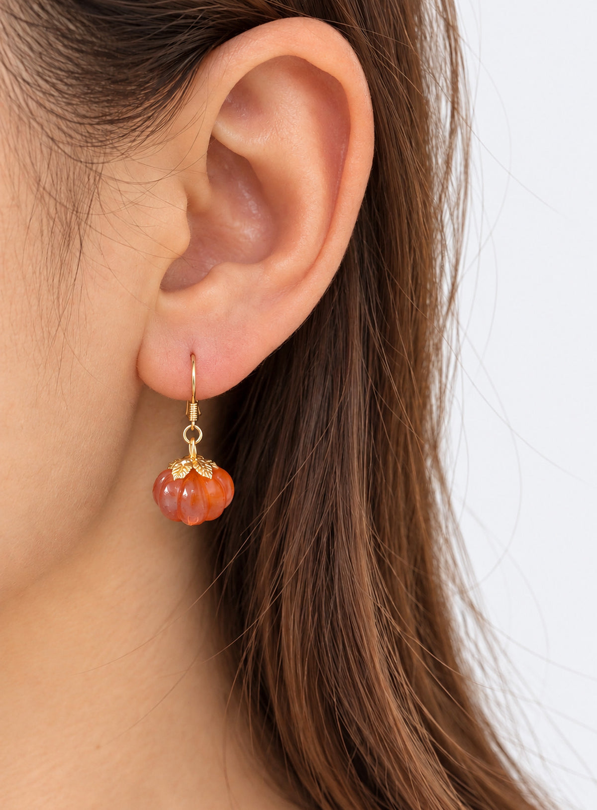 Pair of translucent orange pumpkin earrings with metal leaf details and curved ear hooks