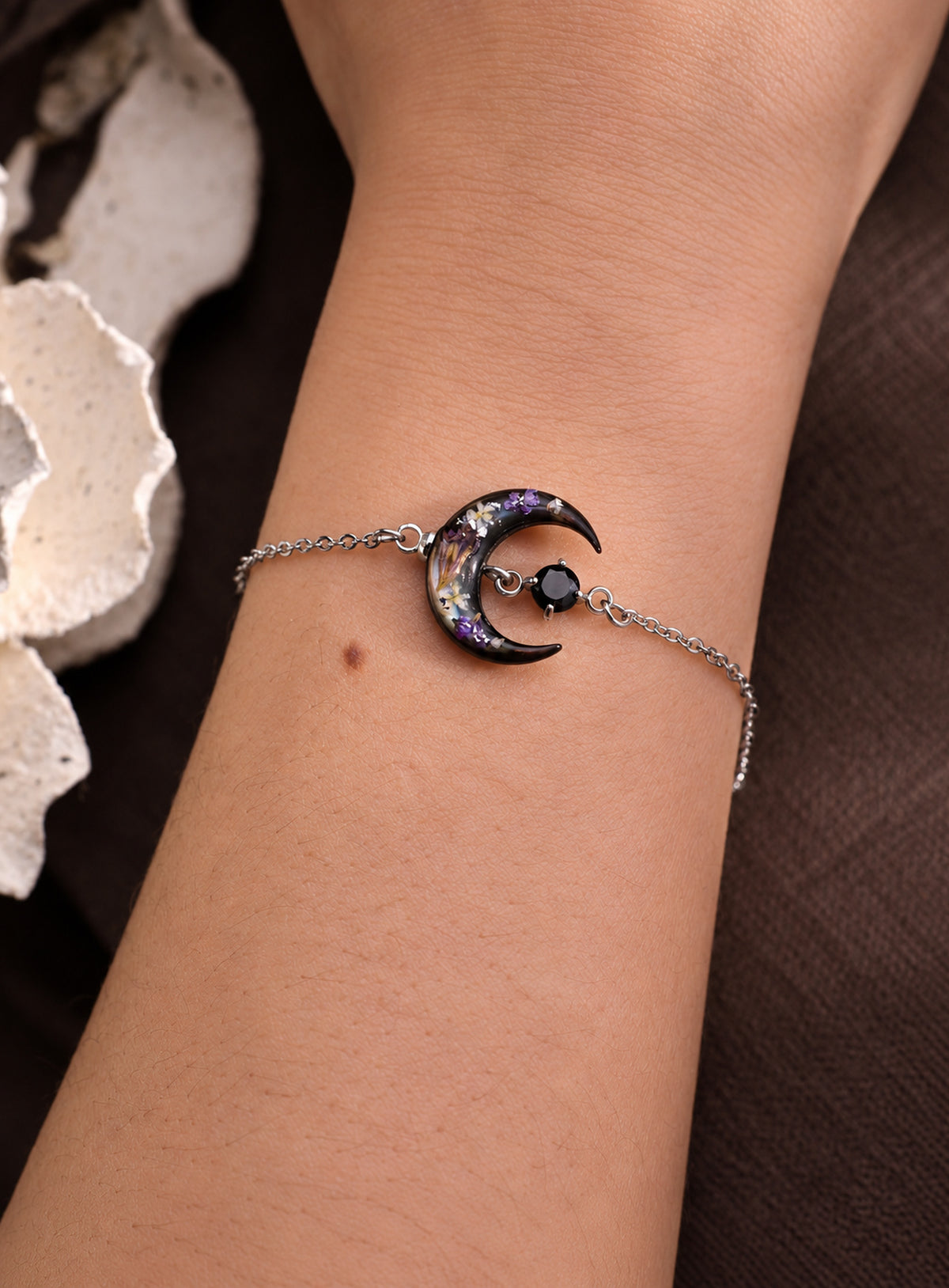 Silver-finish chain bracelet with a dark shell crescent, purple flowers and a black stone accent.