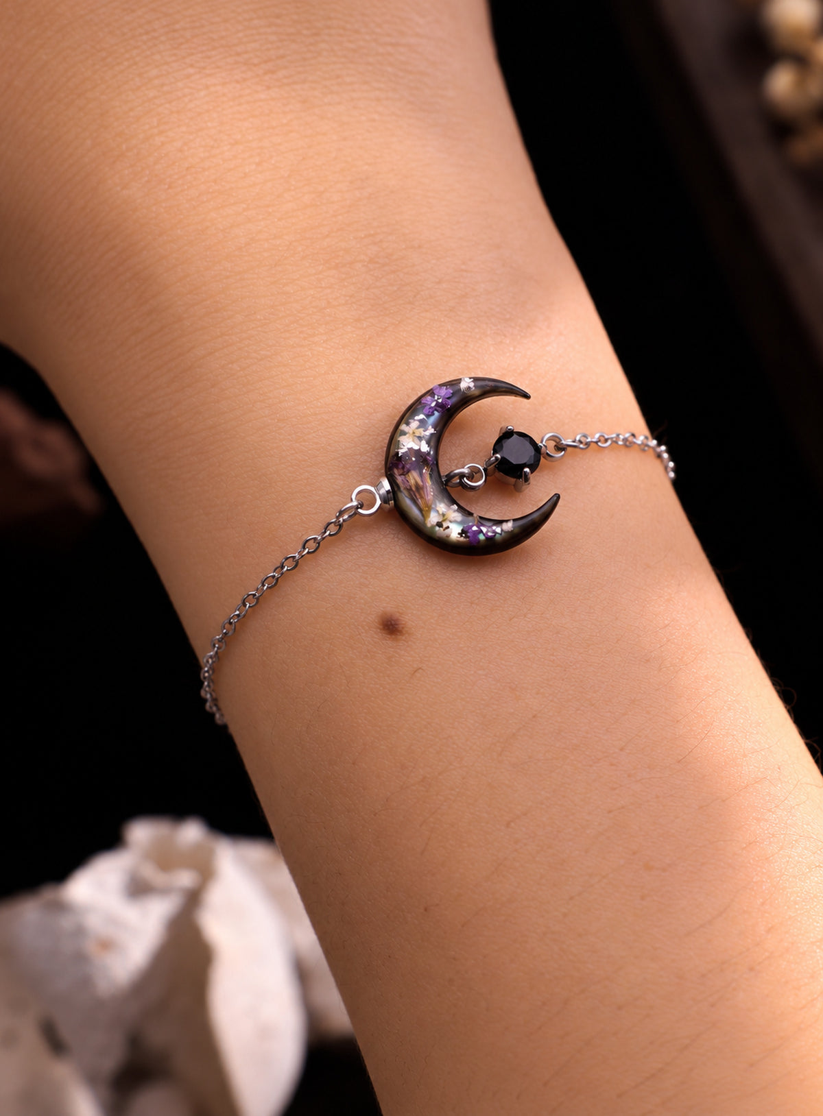 Silver-finish chain bracelet with a dark shell crescent, purple flowers and a black stone accent.