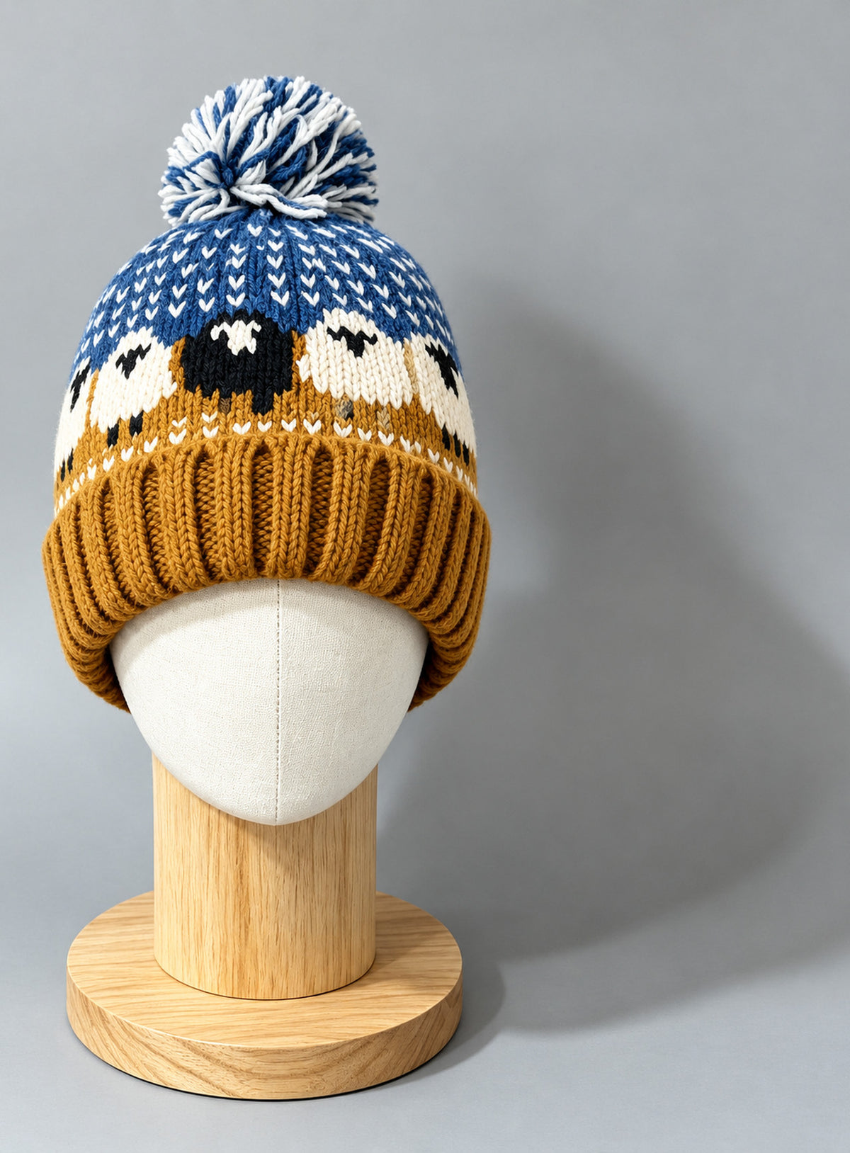 Bright blue pom-pom beanie with ochre ribbed cuff and black-and-white sheep motifs