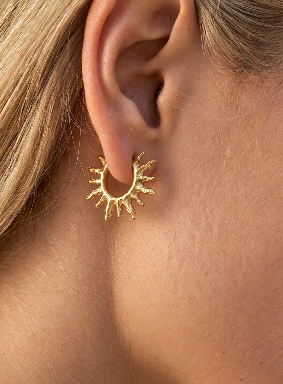 Gold-tone round hoop earrings with pointed sunburst rays around the perimeter